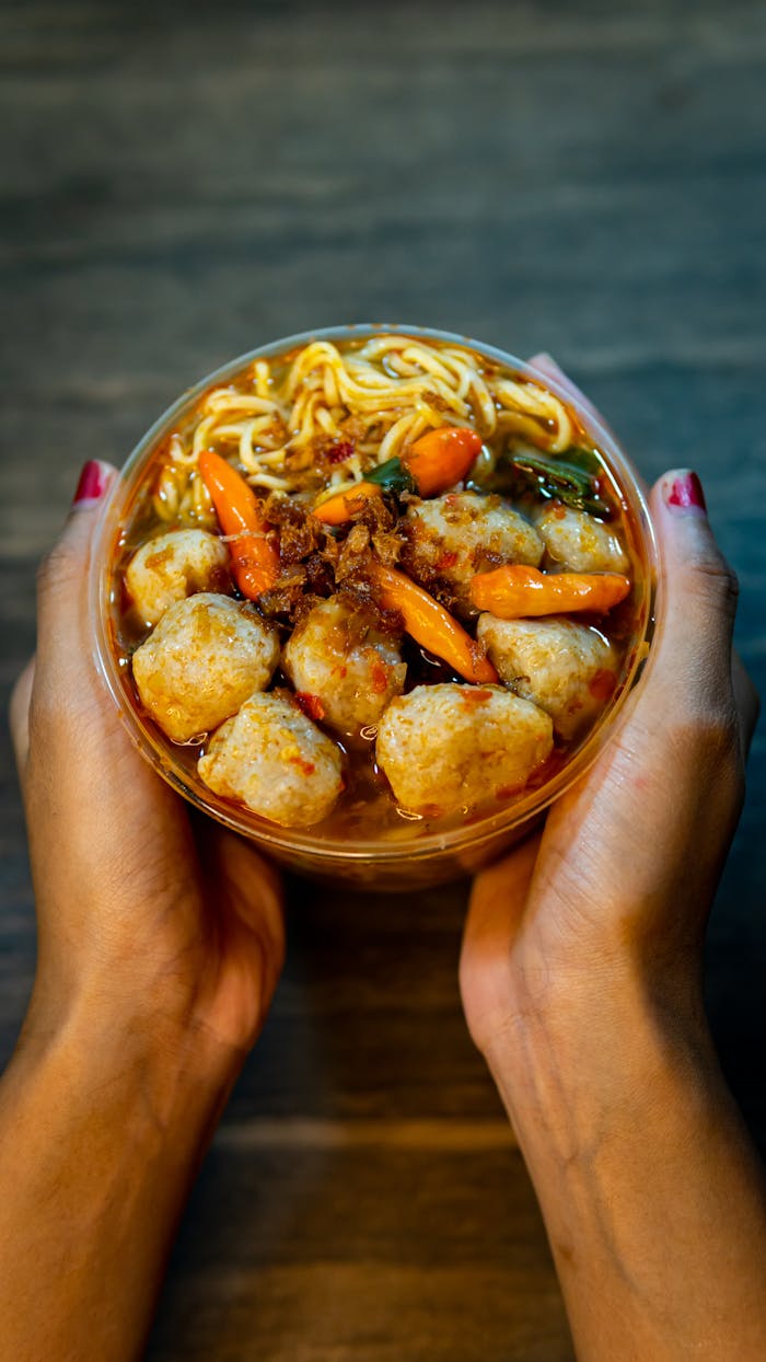 A close-up of Indonesian meatball noodle soup held in hands, showcasing vibrant spices and flavors.