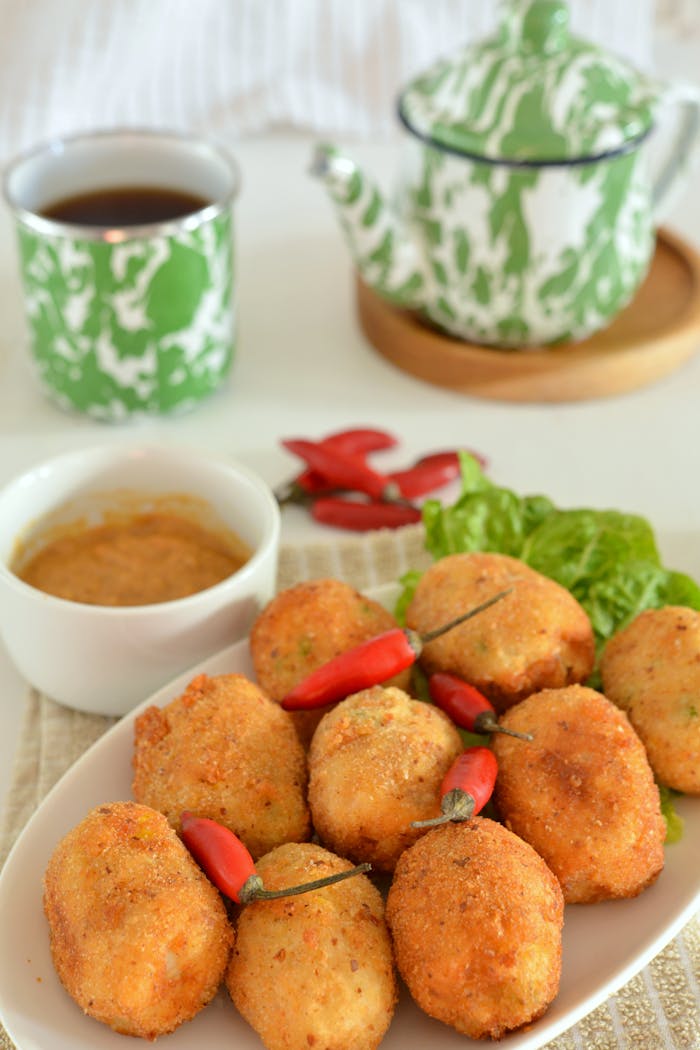 gallery-4 Close-up of fried croquettes with chili peppers, tea, and sauce on a table.